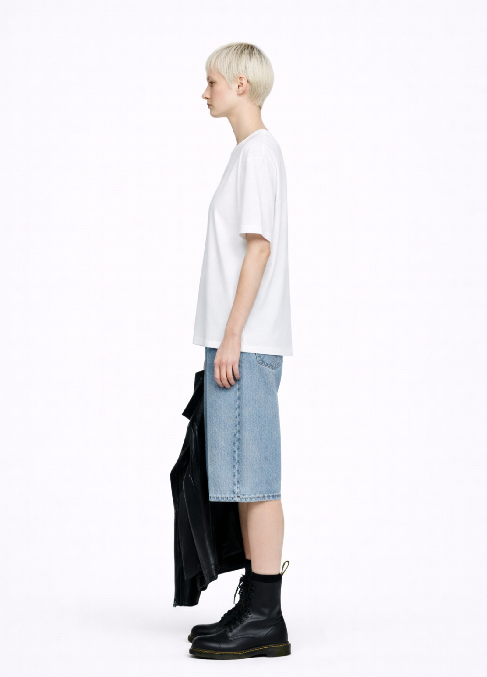 Blond, short hair girl wearing a white Northwind casual storm of wolves t-shirt with Northwind logo embroidered on the chest, blue denim Carhartt oversized shorts, black belt, and black Dr. Martens boots on a white background