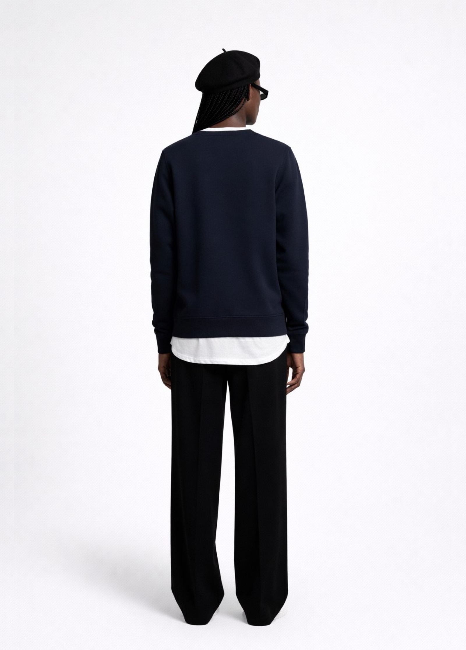 Black woman wearing a french navy blue Northwind sweatshirt black pants, and a black beret on a white background