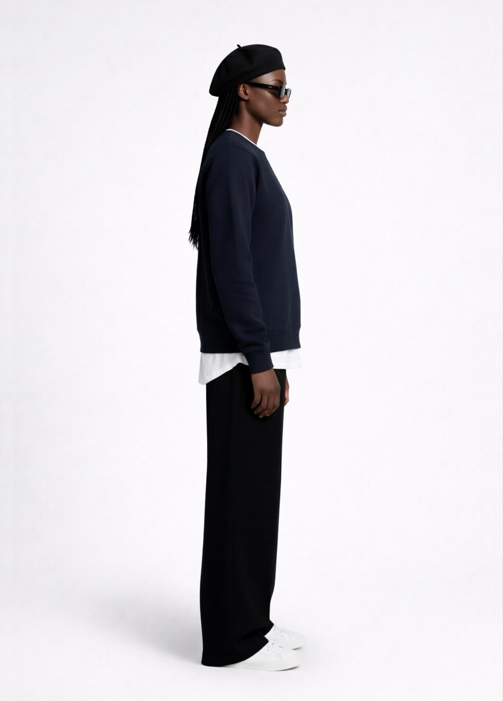 Black woman wearing a french navy blue Northwind sweatshirt with Northwind storm of wolves embroidered logo on the chest, black pants, and a black beret on a white background