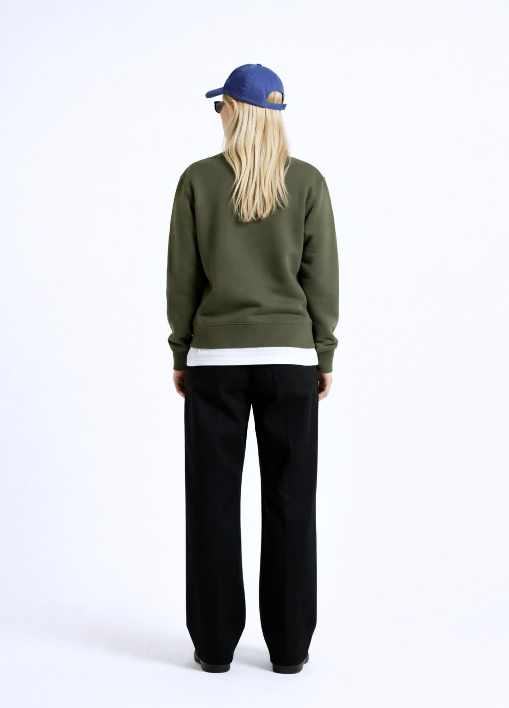 Woman wearing an olive khaki green Northwind sweatshirt with Northwind storm of wolves embroidered logo on the chest, black pants, and a blue cap on a white background