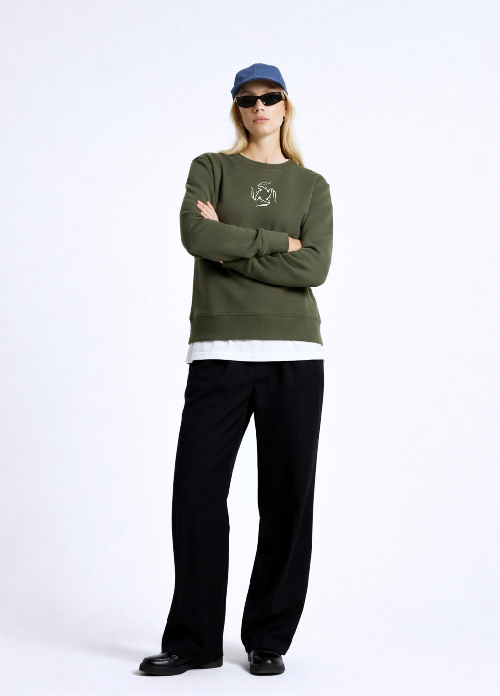 Woman wearing an olive khaki green Northwind sweatshirt with Northwind storm of wolves embroidered logo on the chest, black pants, and a blue cap on a white background