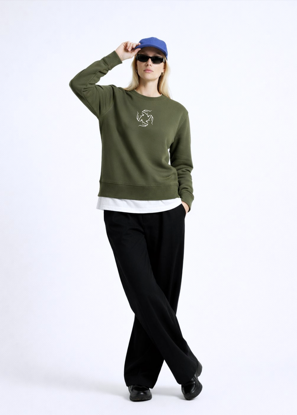 Person wearing an olive khaki green Northwind sweatshirt with Northwind storm of wolves embroidered logo on the chest, black pants, and a blue cap on a white background