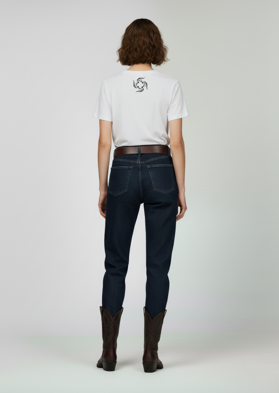 Person wearing a white Northwind t-shirt with a logo, dark jeans, and brown boots on a plain background