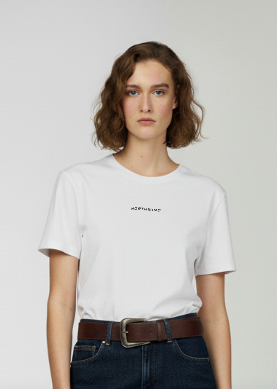 Person wearing a white Northwind t-shirt with text and dark jeans on a plain background