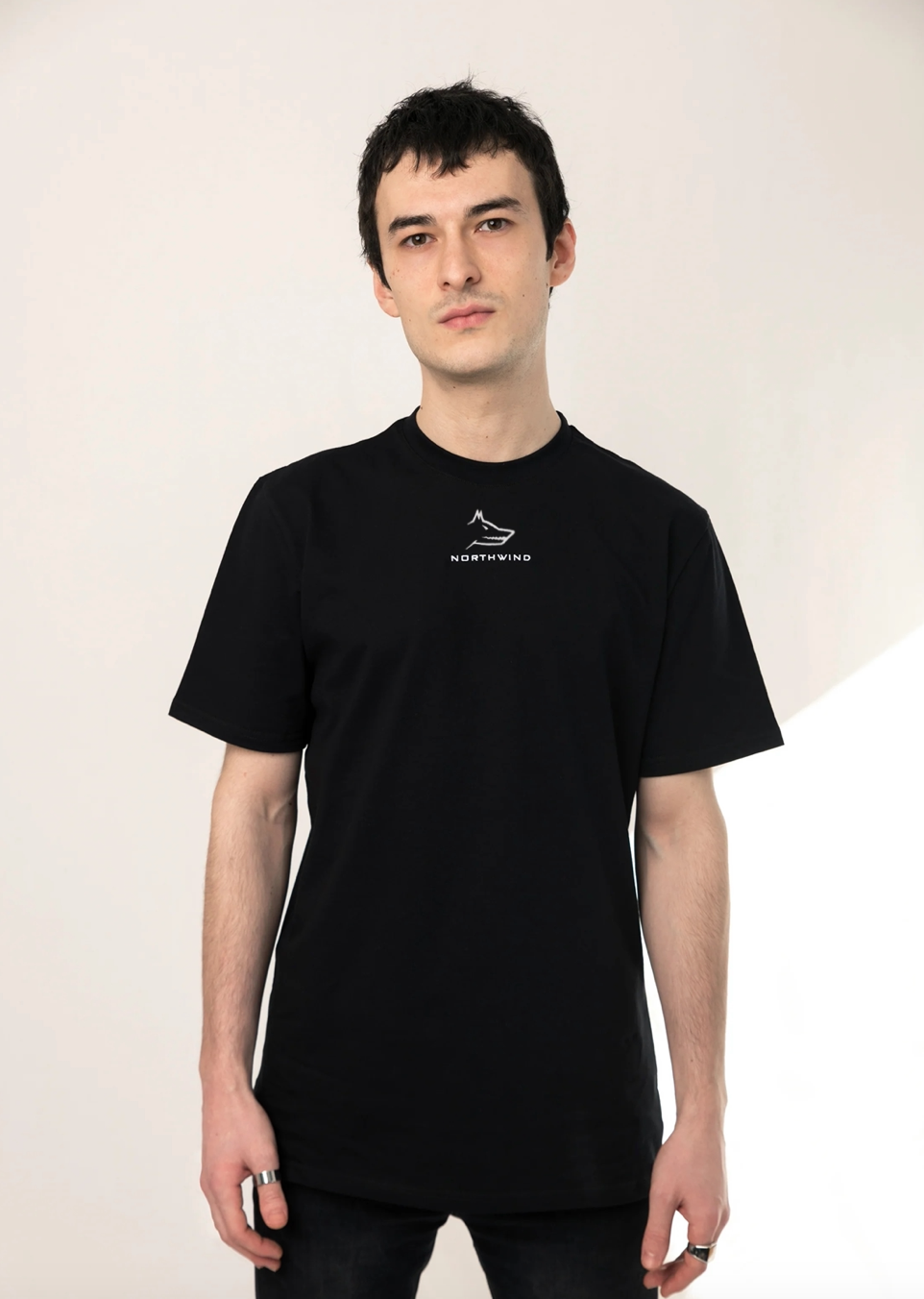 Person wearing a Northwind casual black t-shirt with Northwind embroidery wolf logo on a light background