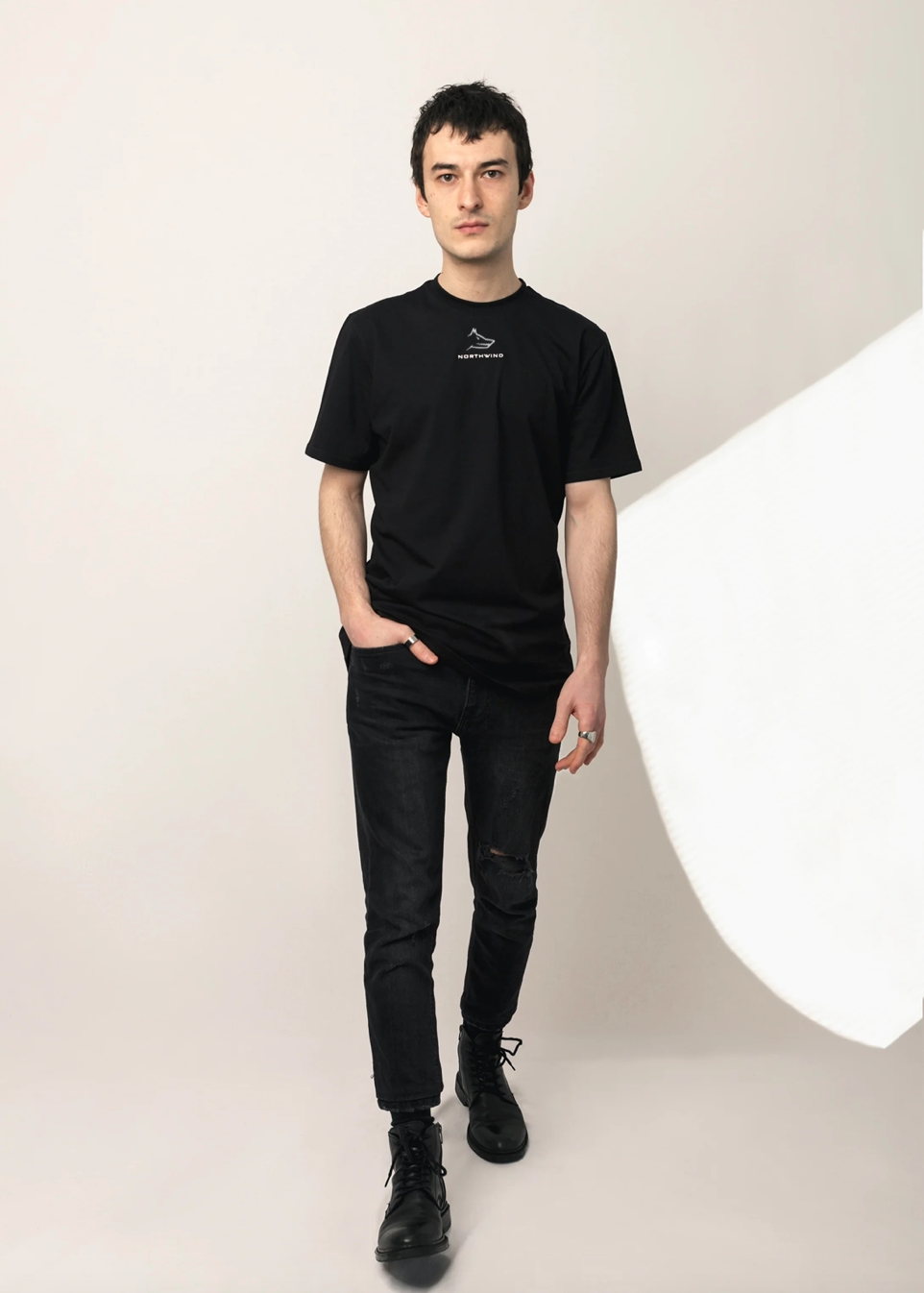 Person wearing a black t-shirt with a logo and black jeans on a white background