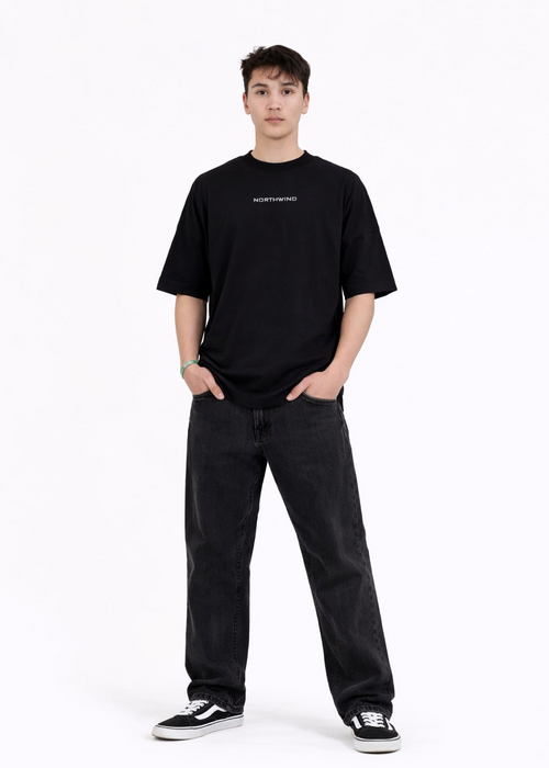 Young adult wearing a Northwind oversized organic cotton black t-shirt with Northwind embroidered on the chest, Carhartt pants, black Vans shoes