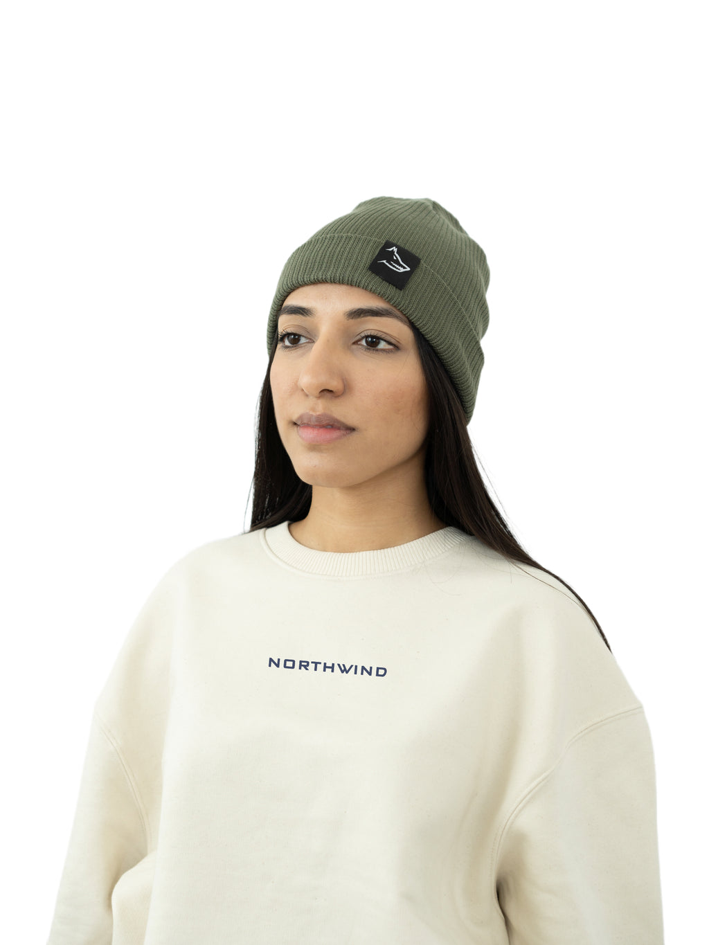 woman wearing a olive green organic cotton beanie with a Northwind wolf logo, and a beige organic oversize Northwind sweatshirt with embroidered logo on the chest