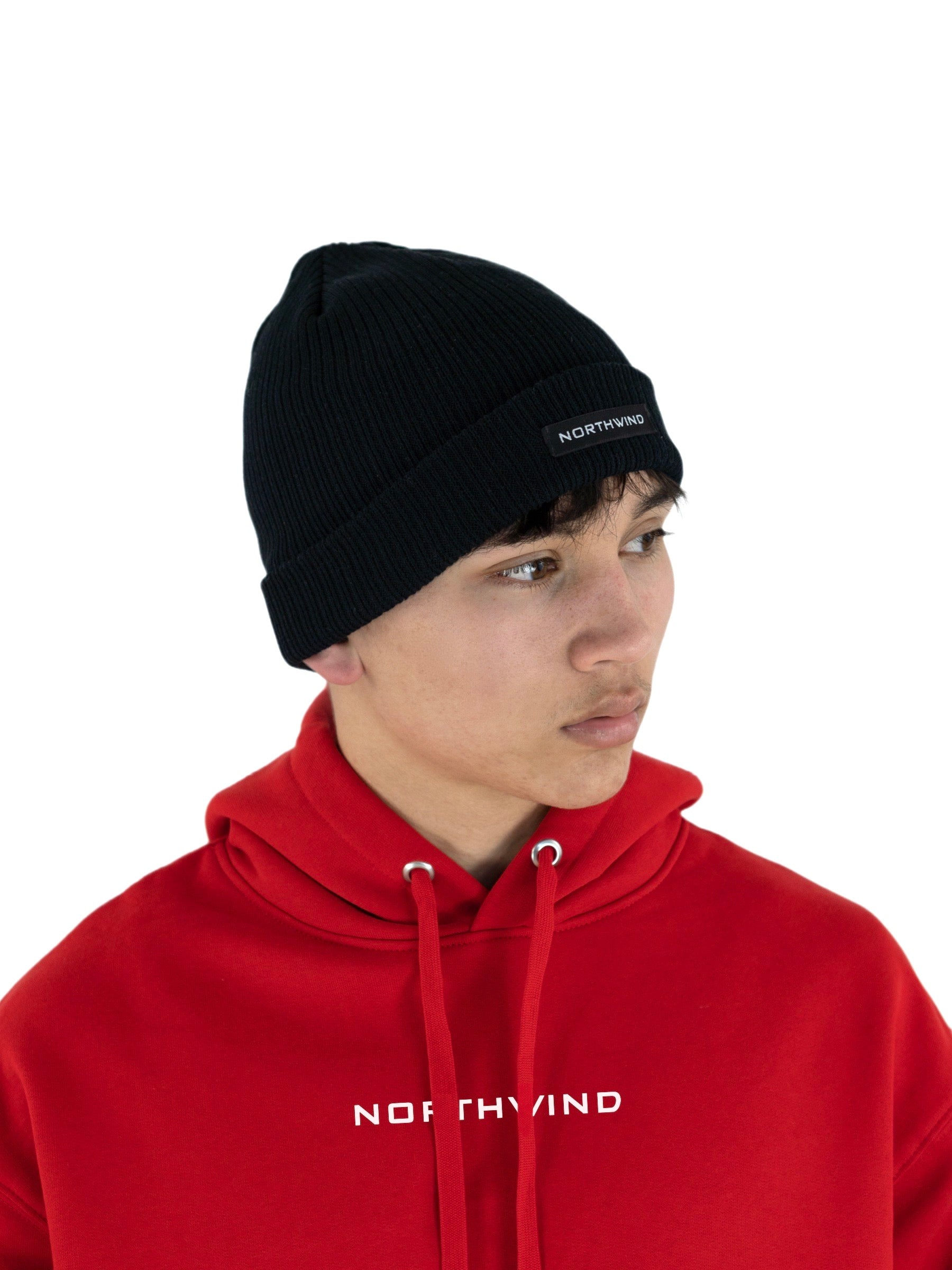 Man wearing a black organic cotton beanie with a Northwind logo, and a red organic cotton oversize heavy Northwind hoodie with embroidered logo on the chest
