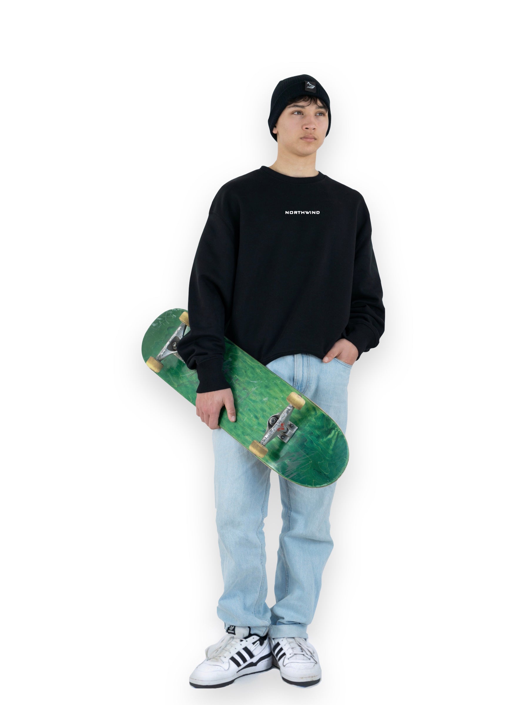 Man wearing a black organic cotton beanie with a Northwind wolf logo, and a black oversize heavy Northwind sweatshirt with embroidered logo on the chest holding a skate board