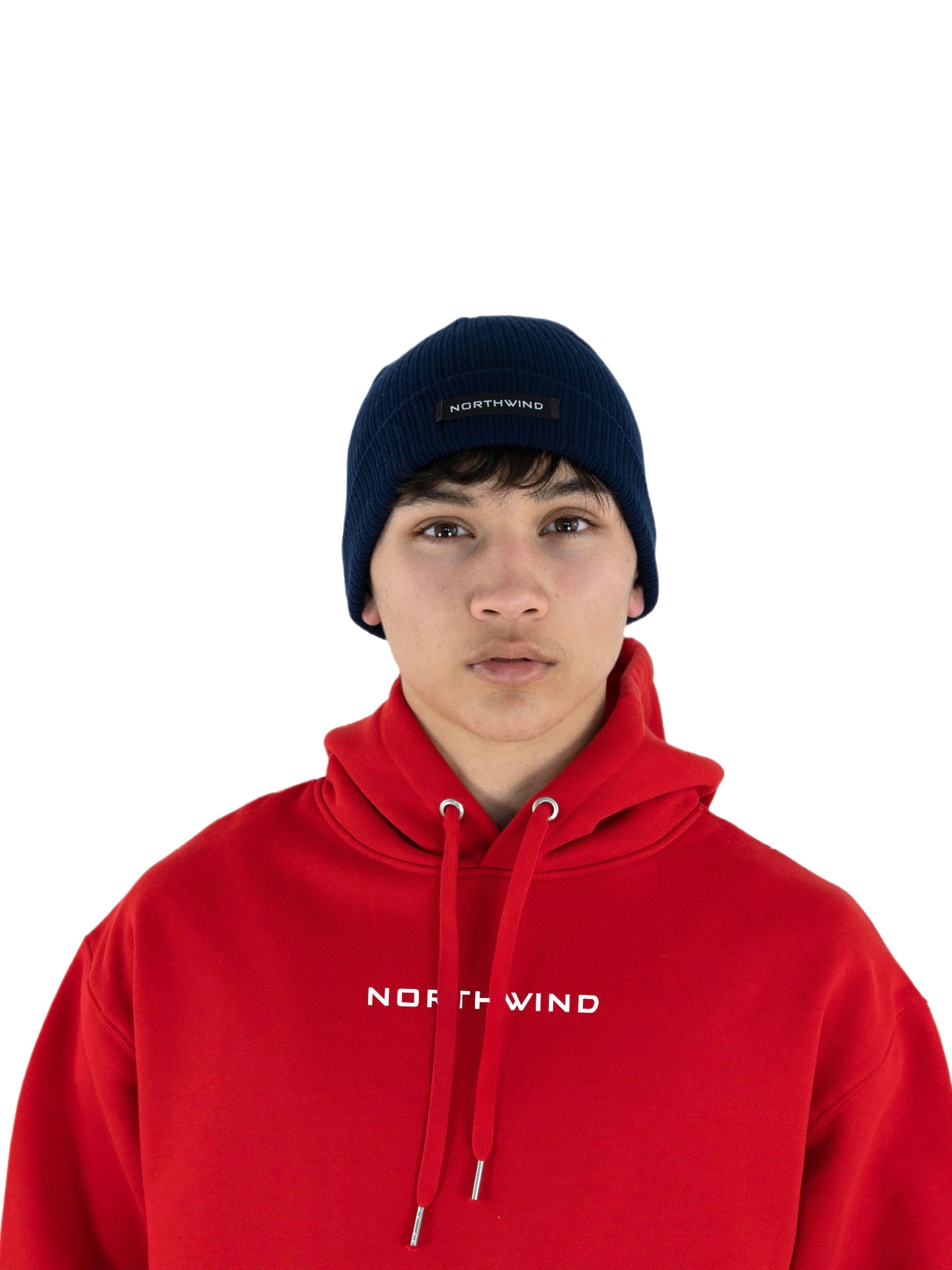 Man wearing a navy blue organic cotton beanie with a Northwind logo, and a red organic cotton oversize heavy Northwind hoodie with embroidered logo on the chest