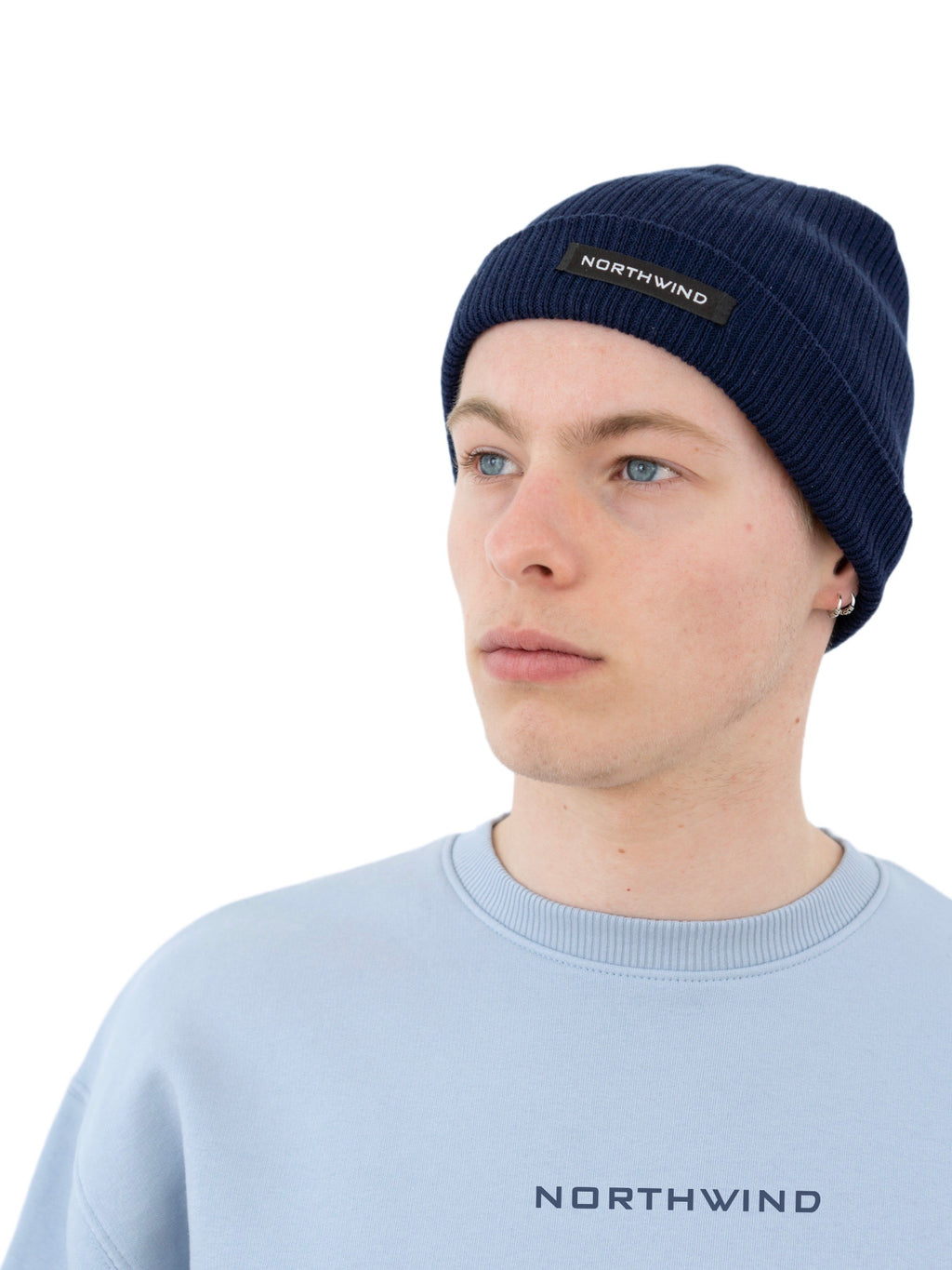 Man wearing a navy blue organic cotton beanie with a Northwind logo, and a sky blue Northwind oversize organic cotton sweatshirt with Northwind logo on the chest