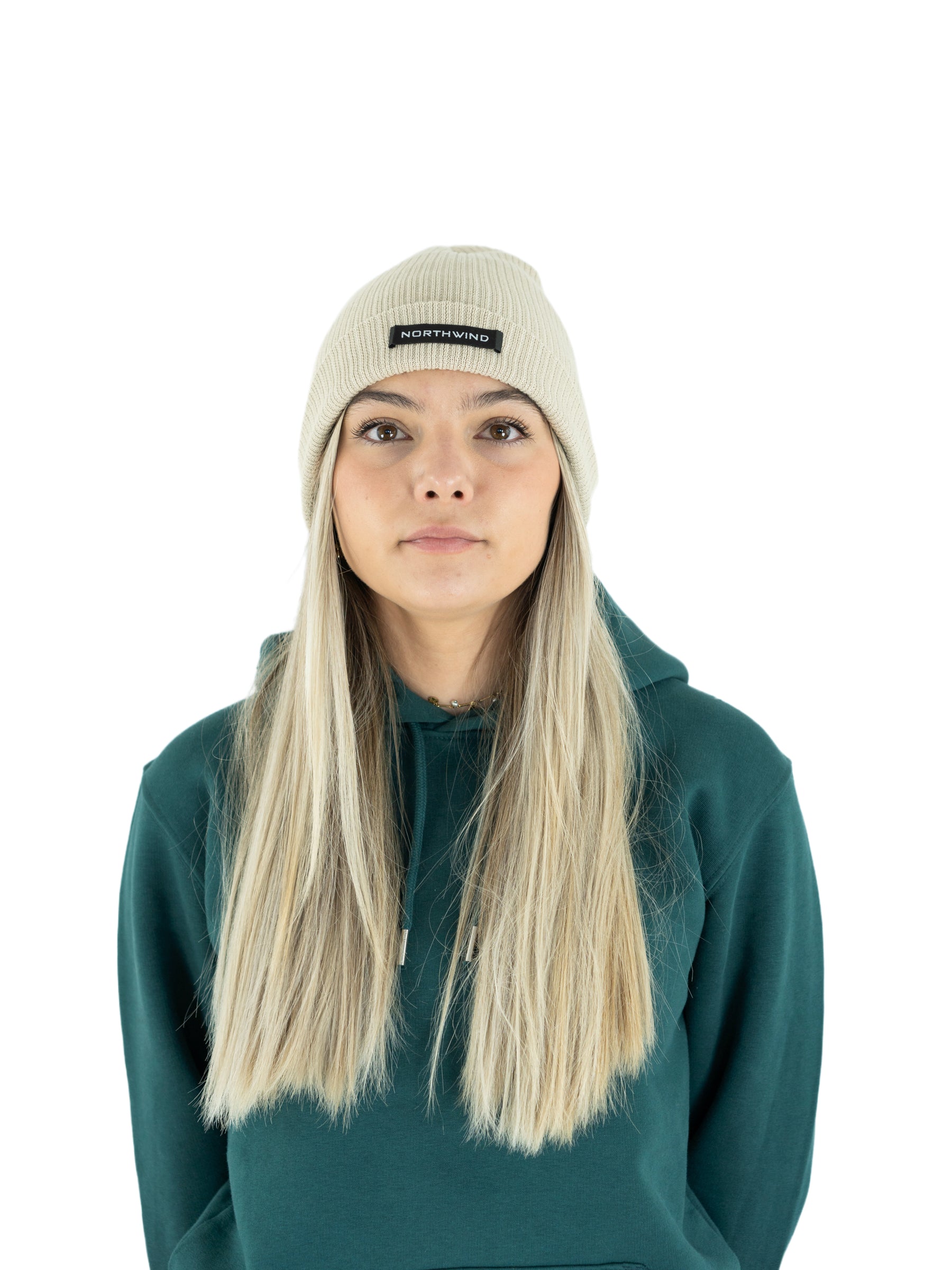 Woman wearing a beige organic cotton beanie with a Northwind brand logo, and a green Northwind hoodie on a white background
