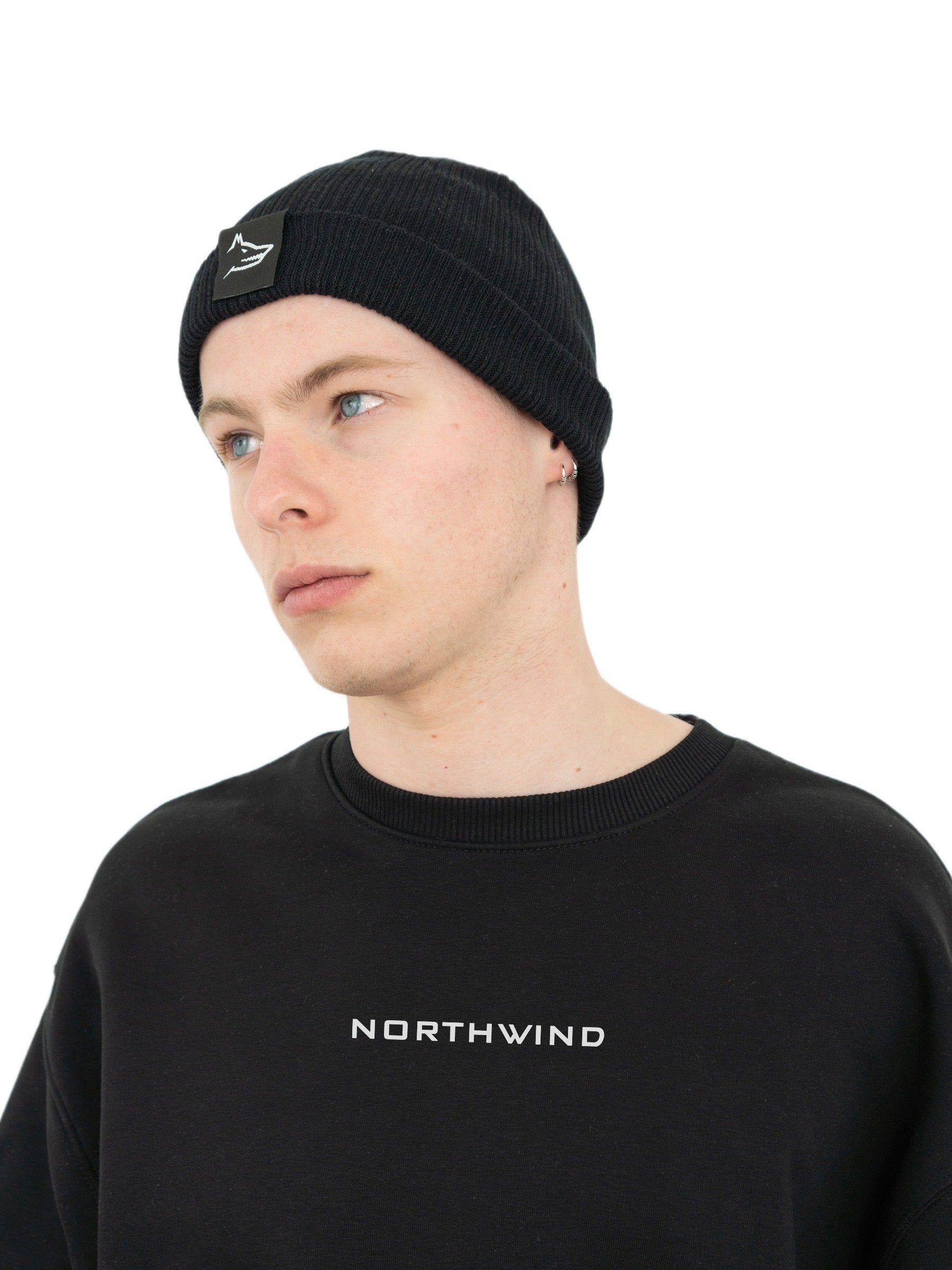 Man wearing a black organic cotton beanie with a Northwind wolf logo, and a black oversize heavy Northwind sweatshirt with embroidered logo on the chest
