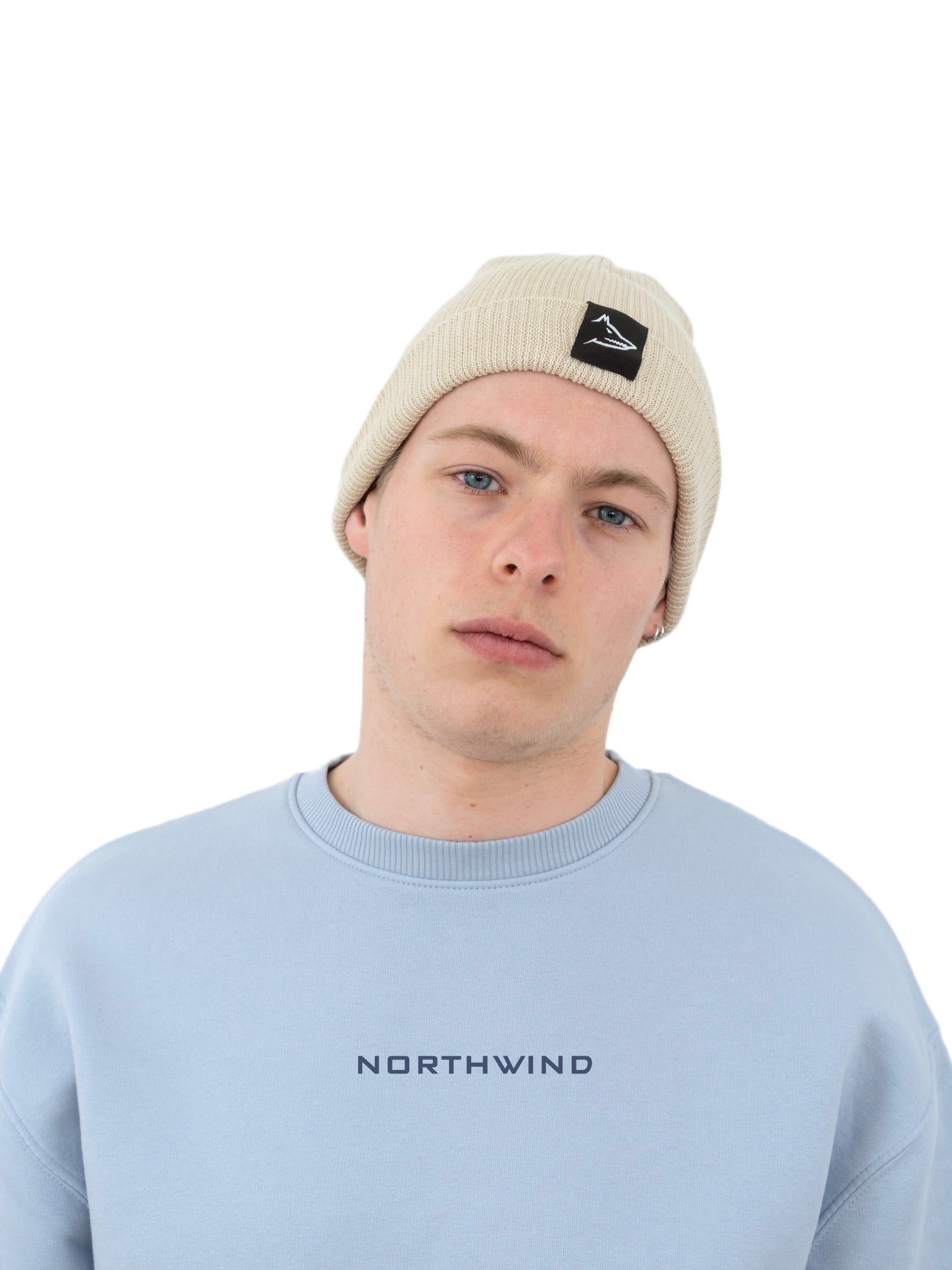 Man wearing a beige organic cotton beanie with a Northwind wolf logo, and a sky blue Northwind oversize organic cotton sweatshirt with Northwind logo on the chest