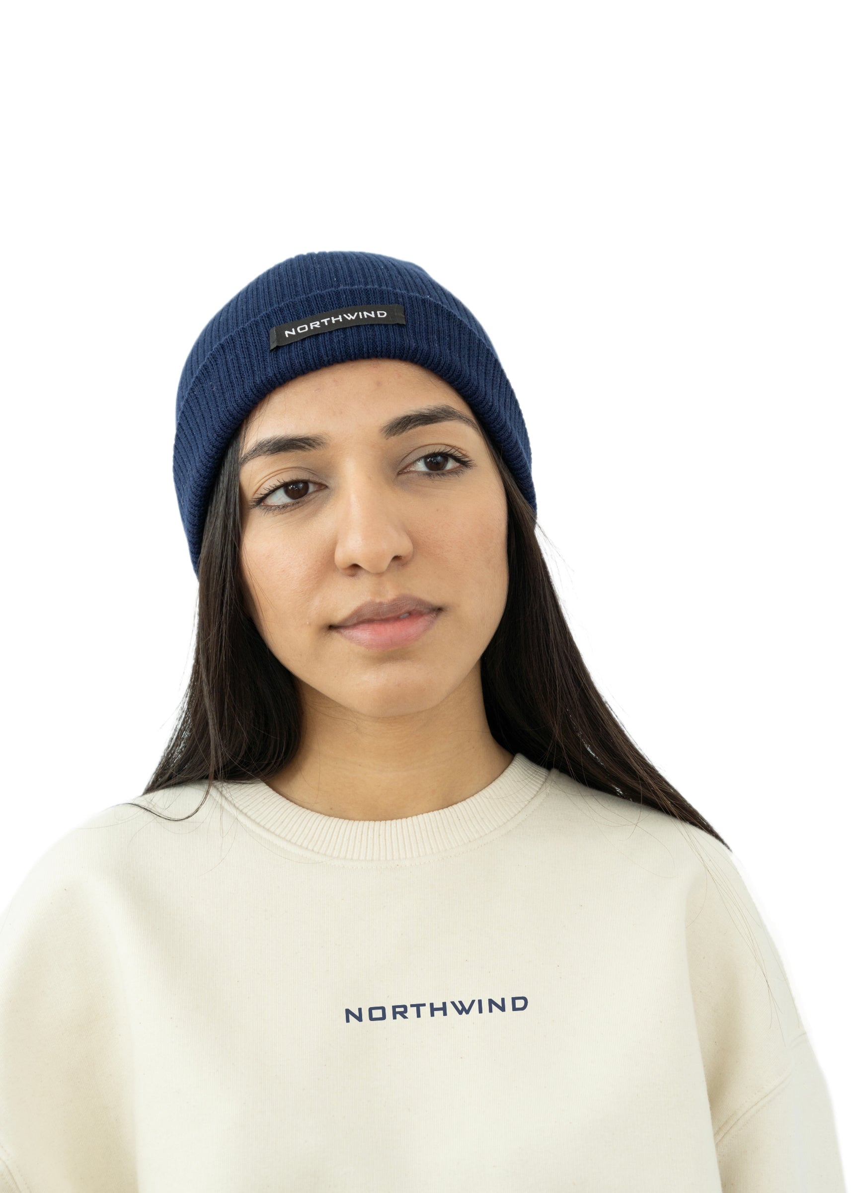 woman wearing a navy blue organic cotton beanie with a Northwind brand logo, and a beige Northwind  oversize organic cotton heavy sweatshirt with embroidered logo on the chest